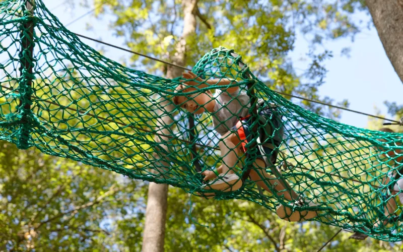 Un garçon en train de faire un parcours aventure dans un filet dans les arbres